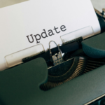 Uma fotografia com iluminação quente e acolhedora em estilo "flat lay". No centro, um caderno de capa de couro marrom (estilo traveler's notebook) está fechado com um elástico. Sobre ele, repousa uma caneta tinteiro preta com detalhes em prata, onde se lê a inscrição "Kaweco AL Sport". O caderno está apoiado sobre um tecido rústico de juta em uma mesa de madeira escura, criando uma atmosfera de escrita clássica e reflexiva.