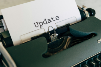 Uma fotografia com iluminação quente e acolhedora em estilo "flat lay". No centro, um caderno de capa de couro marrom (estilo traveler's notebook) está fechado com um elástico. Sobre ele, repousa uma caneta tinteiro preta com detalhes em prata, onde se lê a inscrição "Kaweco AL Sport". O caderno está apoiado sobre um tecido rústico de juta em uma mesa de madeira escura, criando uma atmosfera de escrita clássica e reflexiva.