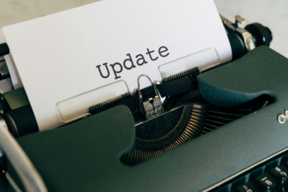 Uma fotografia com iluminação quente e acolhedora em estilo "flat lay". No centro, um caderno de capa de couro marrom (estilo traveler's notebook) está fechado com um elástico. Sobre ele, repousa uma caneta tinteiro preta com detalhes em prata, onde se lê a inscrição "Kaweco AL Sport". O caderno está apoiado sobre um tecido rústico de juta em uma mesa de madeira escura, criando uma atmosfera de escrita clássica e reflexiva.