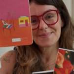 A imagem apresenta a psicanalista e colunista Carolina Delboni, figura central no debate sobre educação e comportamento adolescente mencionado em seu texto. Descrição Detalhada: A figura central: Carolina aparece em primeiro plano, com um semblante acolhedor e um leve sorriso. Ela usa óculos de armação grossa e avermelhada, que se destacam em seu rosto. Elementos visuais: Ela segura e exibe livros, reforçando sua autoridade no tema educacional. No canto inferior direito, destaca-se claramente a capa de um de seus livros, intitulado "As Dores da Adolescência: Como entender, acolher e cuidar". Composição: A foto tem um estilo intimista e intelectual. O fundo está levemente desfocado, o que direciona toda a atenção para ela e para as obras que simbolizam seu trabalho de orientação para pais e educadores. Simbolismo: A imagem comunica proximidade e cuidado, características que ela defende em seus artigos ao sugerir que a educação dos meninos deve passar pelo acolhimento emocional e pela escuta ativa.