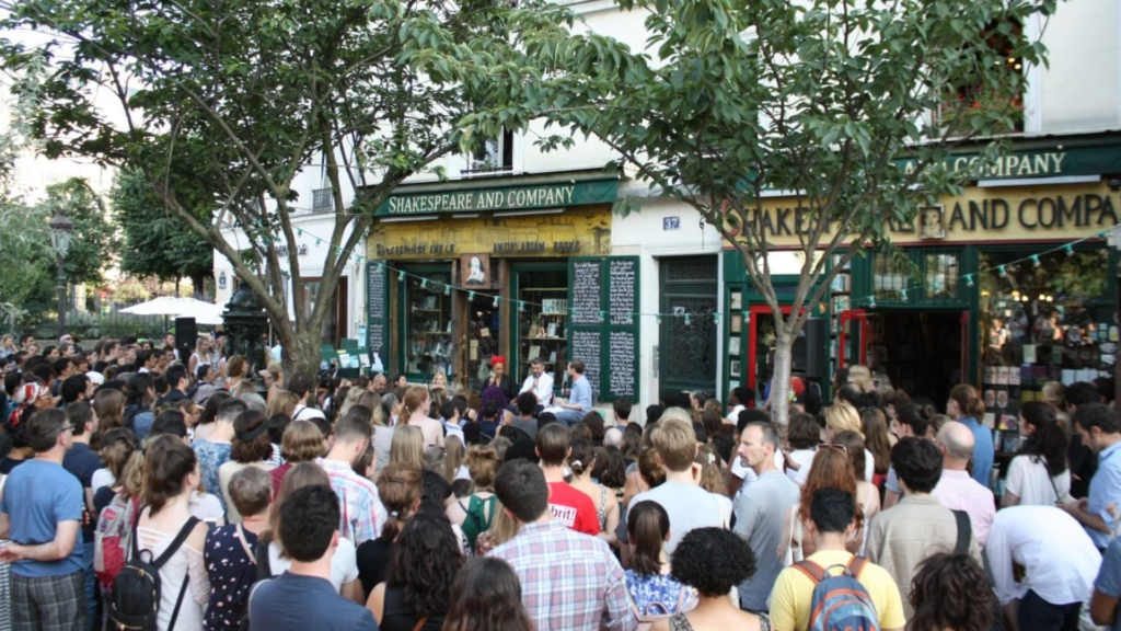 Multidão reunida na rua em frente à livraria Shakespeare and Company, em Paris, durante evento literário ao ar livre. 