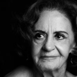 Retrato em preto e branco da atriz brasileira Laura Cardoso, com iluminação dramática vinda da esquerda, destacando as expressões faciais e marcas de idade. Ela olha para o lado com um leve sorriso. O fundo é totalmente escuro.