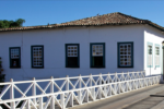 Fachada da Casa Velha da Ponte, na Cidade de Goiás, onde fica o Museu Casa de Cora Coralina: casarão colonial branco com janelas verdes, ao lado de uma ponte de madeira.